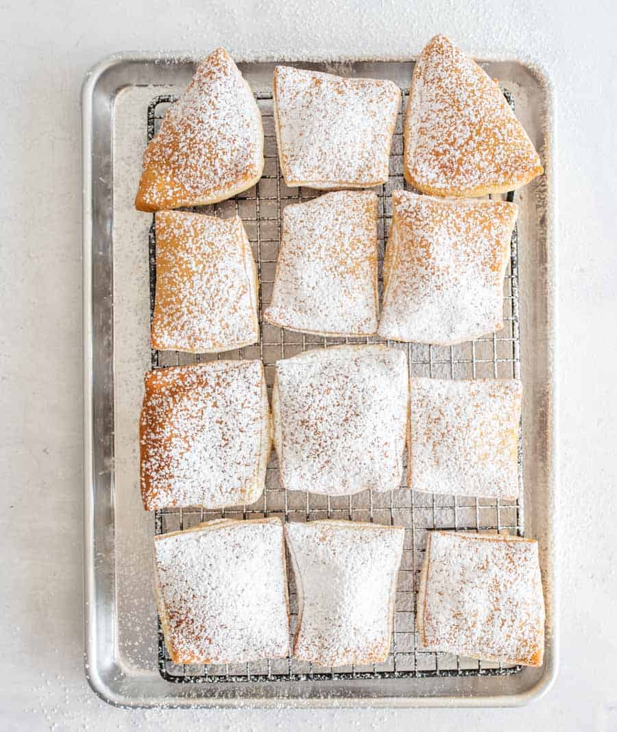 Top view of beignets on a cooling rack dusted with powdered sugar.