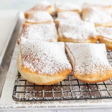 close up of beignets dusted with powdered sugar on a tray