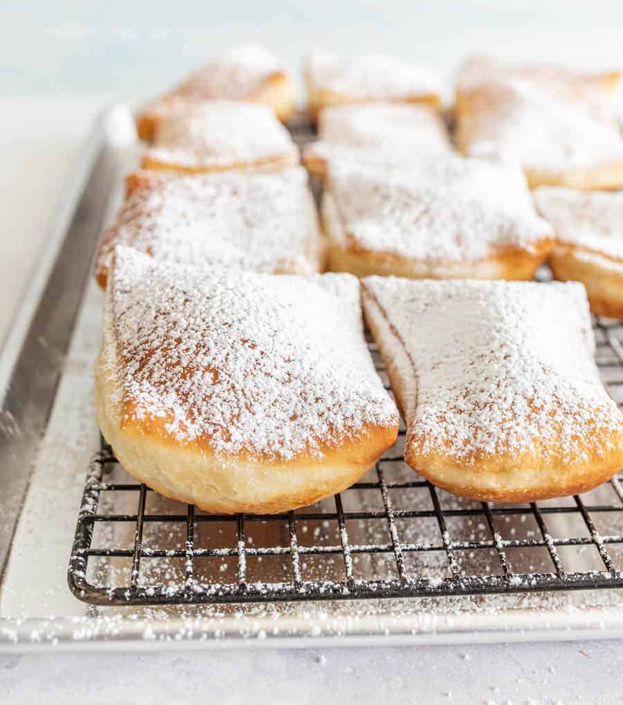 close up of beignets dusted with powdered sugar on a tray