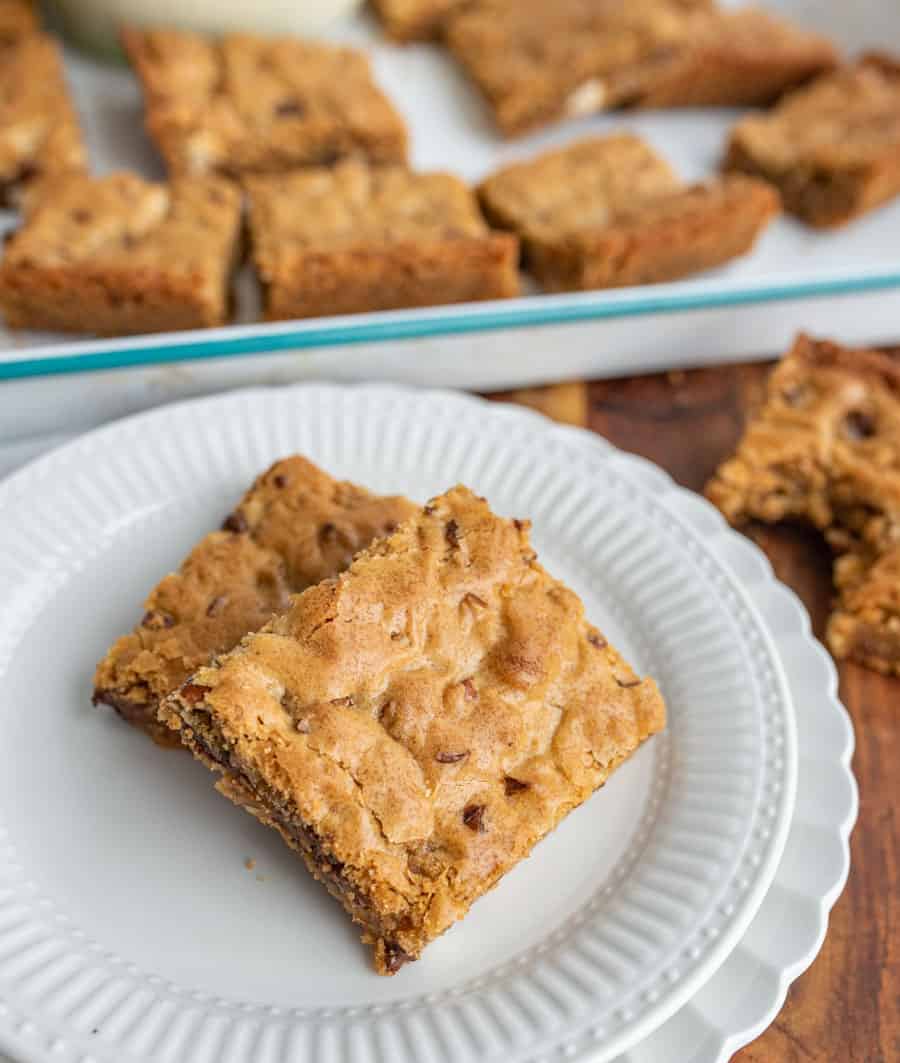 close up of a plate of blondies with a pan of blondies in the background