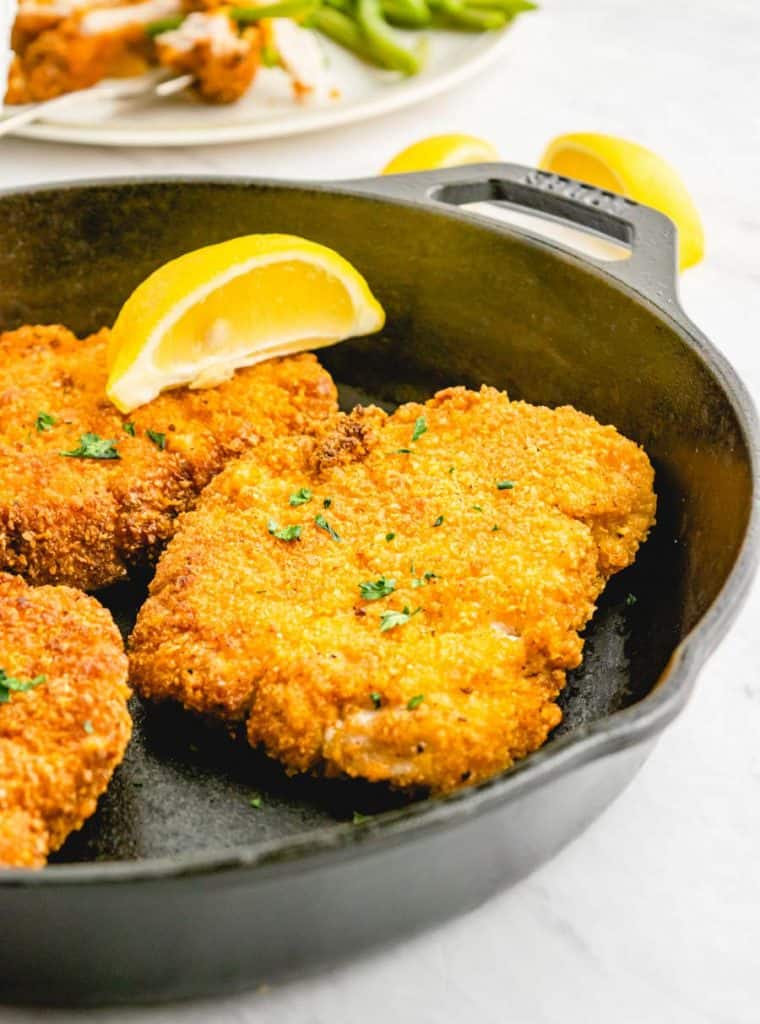 close up picture of crispy fried pork chops in a cast iron skillet with a lemon slice