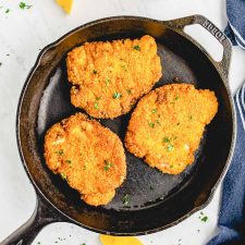 crispy fried pork chops in a cast iron skillet with lemon slices