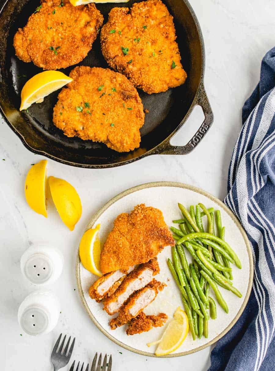 top view of cirspy fried pork chops in a cast iron skillet next to a plate of sliced pork chop and green beans