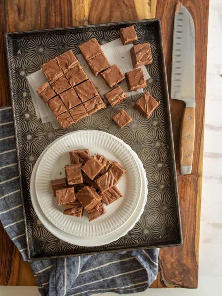 top view of chocolate fudge squares on a plate with fudge squares on a pan and a knife