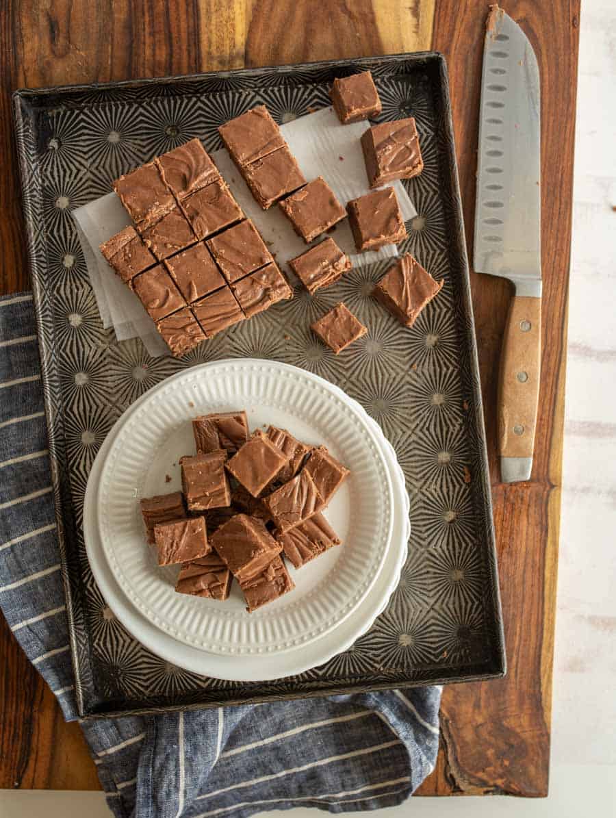 Top view of chocolate fudge squares on a plate with fudge squares on a pan and a knife.