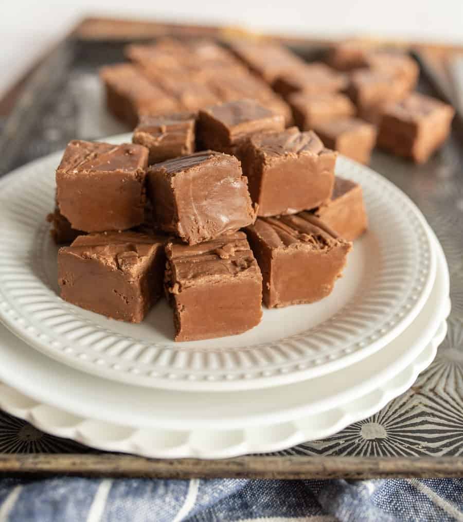 Up close of chocolate fudge squares stacked on a white plate.