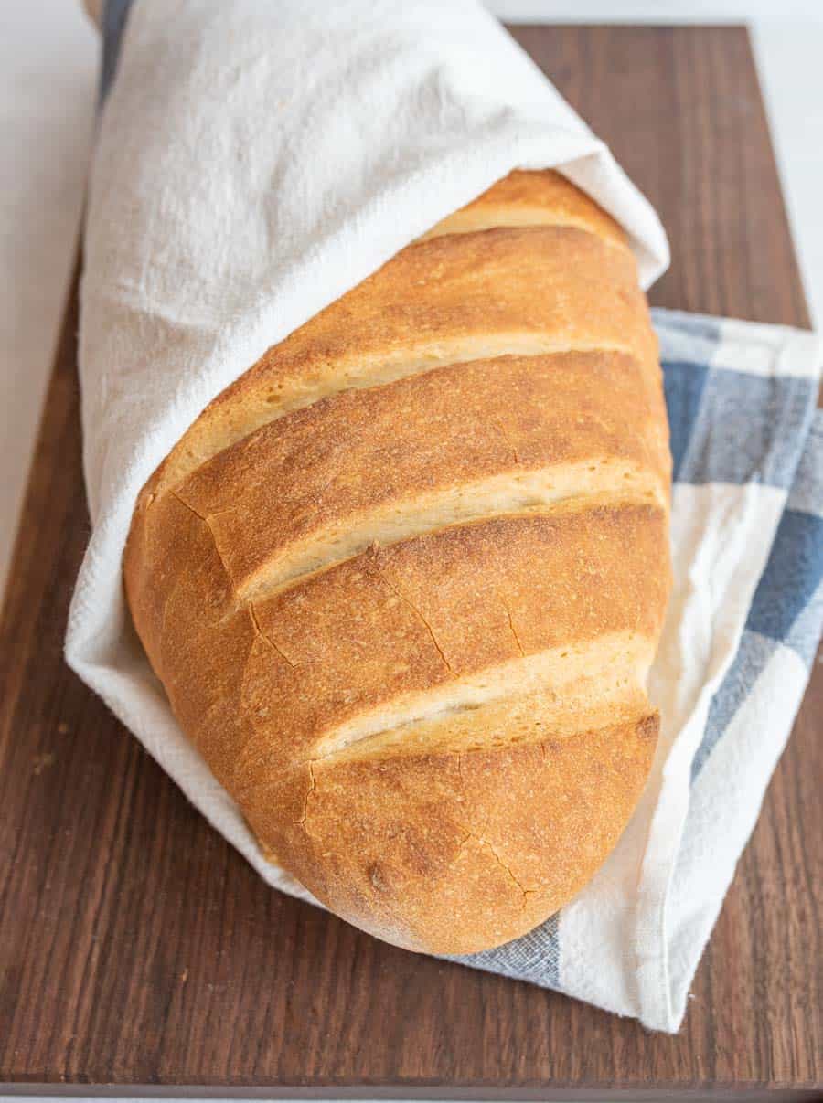 loaf of Italian bread wrapped in a towel on a cutting board