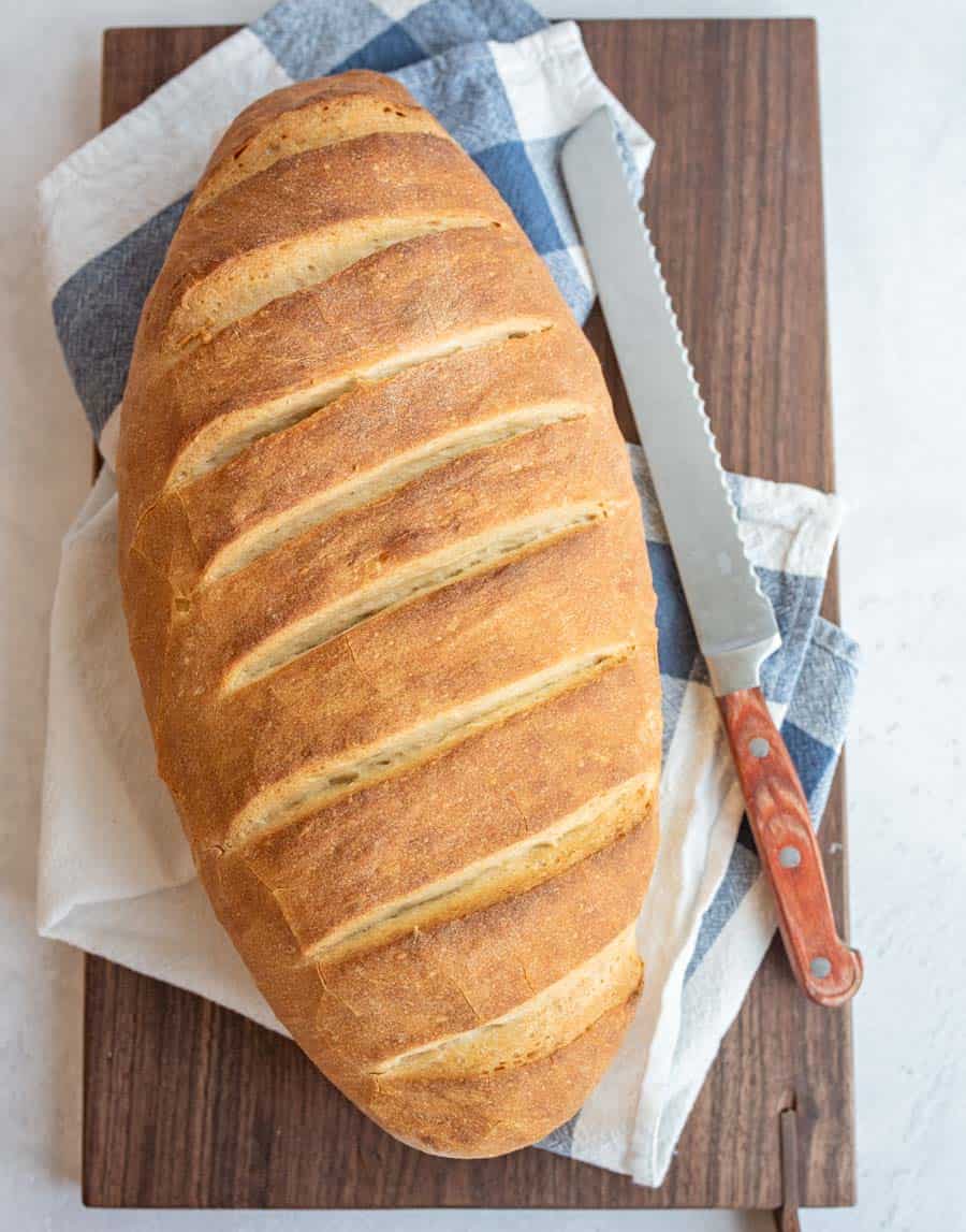 loaf of Italian bread on a towel and cutting board with a knife next to it