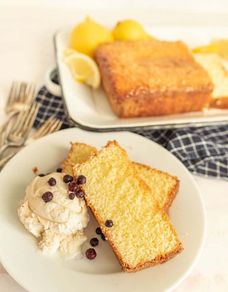Lemon pound cake slices on a plate with ice cream and a lemon pound cake loaf in the background