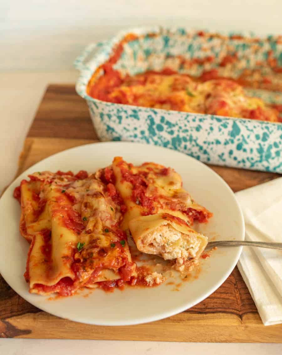A plate of manicotti with a pan of manicotti in the background.