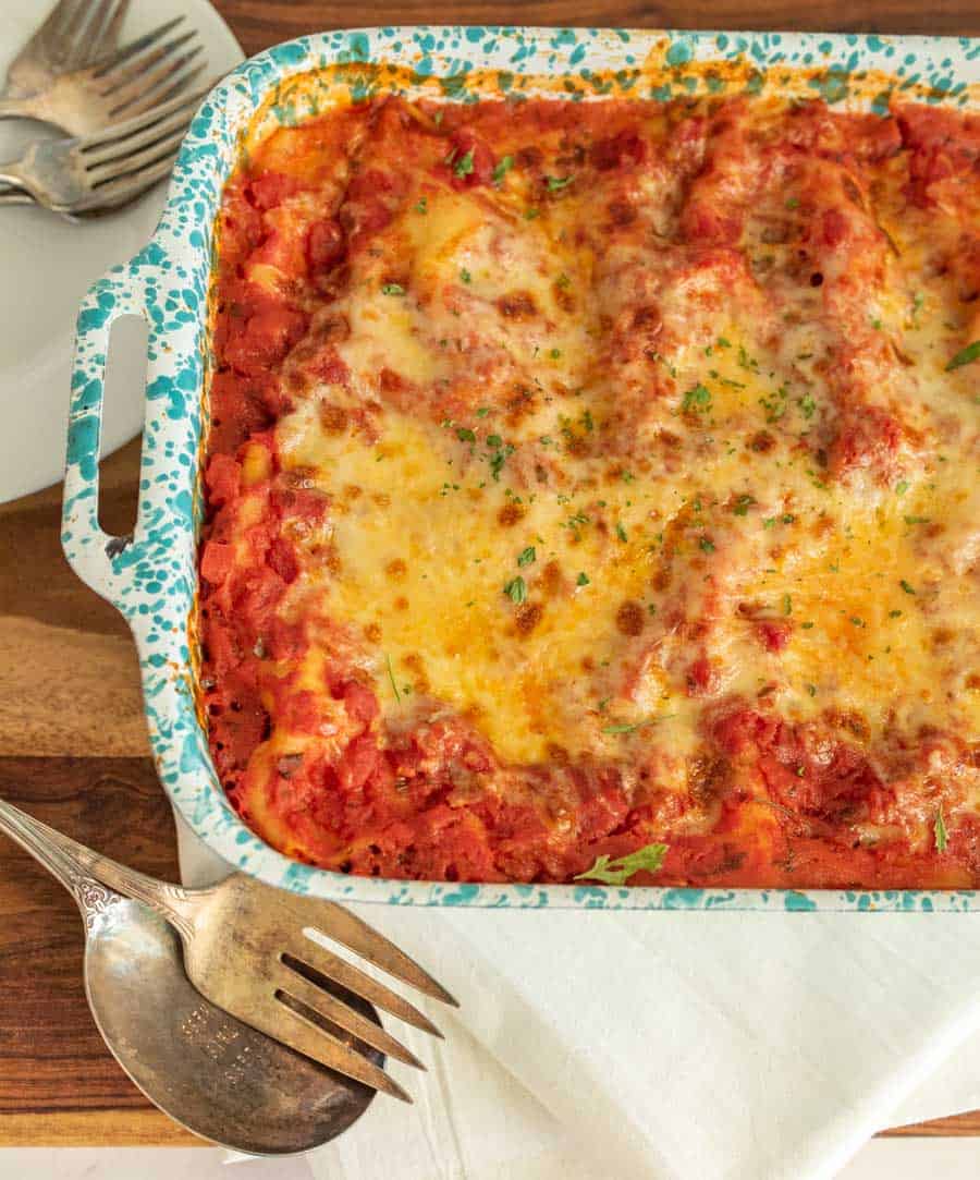 A top view of a pan of baked manicotti with serving utensils next to it.