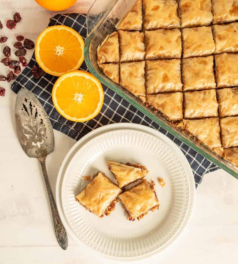 top view of a plate and pan of baklava with oranges and cranberries next to it