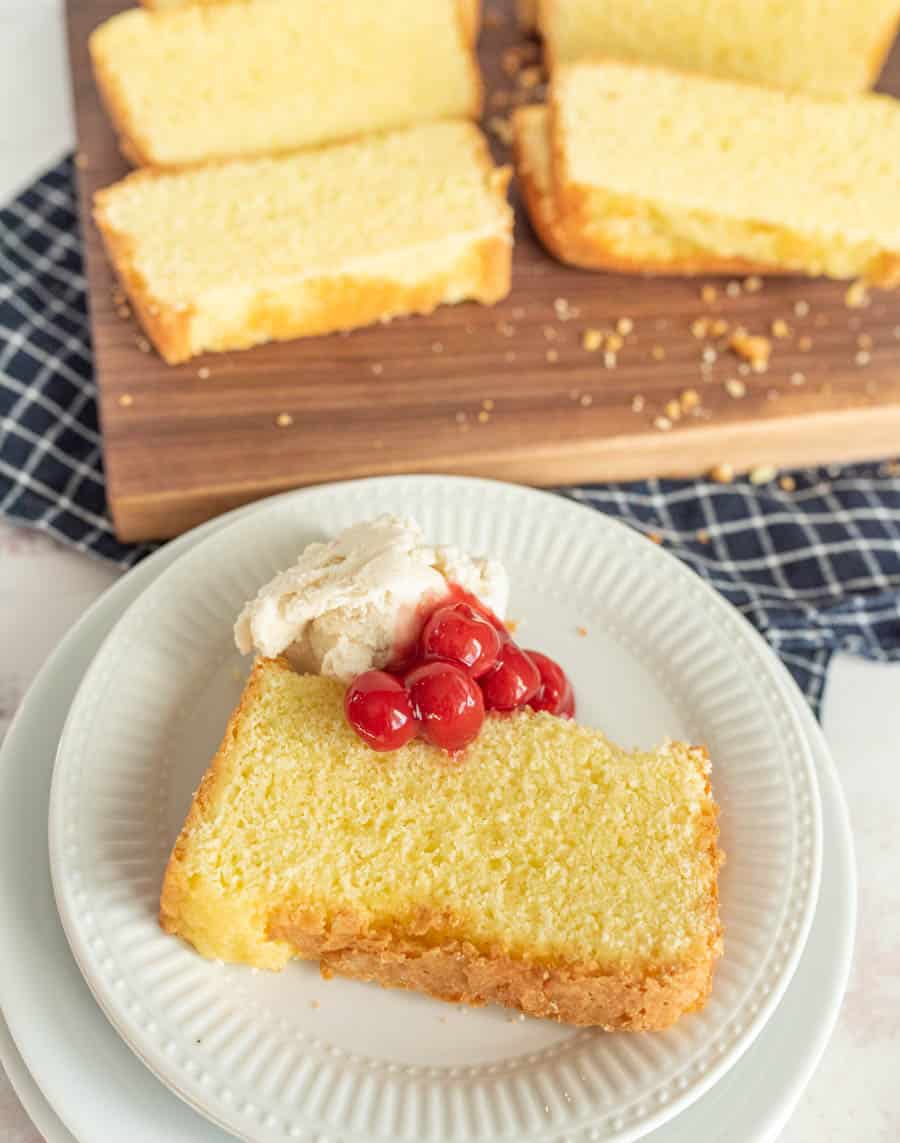 plate of pound cake with ice cream and cherry topping and a cutting board with slices of pound cake in the background