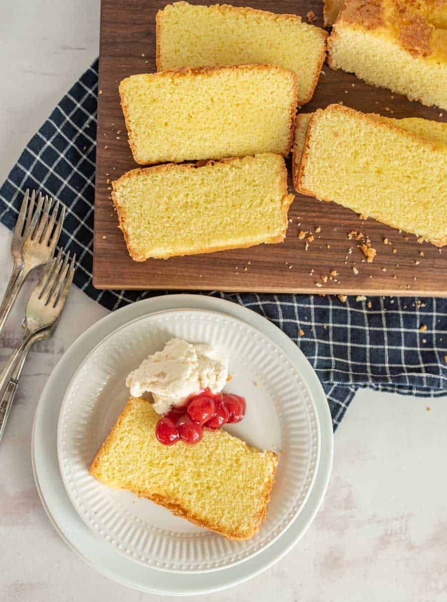 top view of a slice of pound cake with ice cream and cherry topping and a cutting board of slices of pound cake