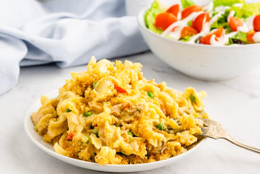 close up picture of a plate of tuna noodle casserole with a bowl of salad in the background