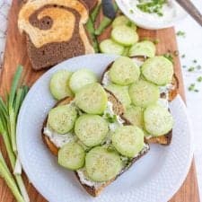 top view of a plate of cucumber sandwiches with the ingredients for them next to the plate