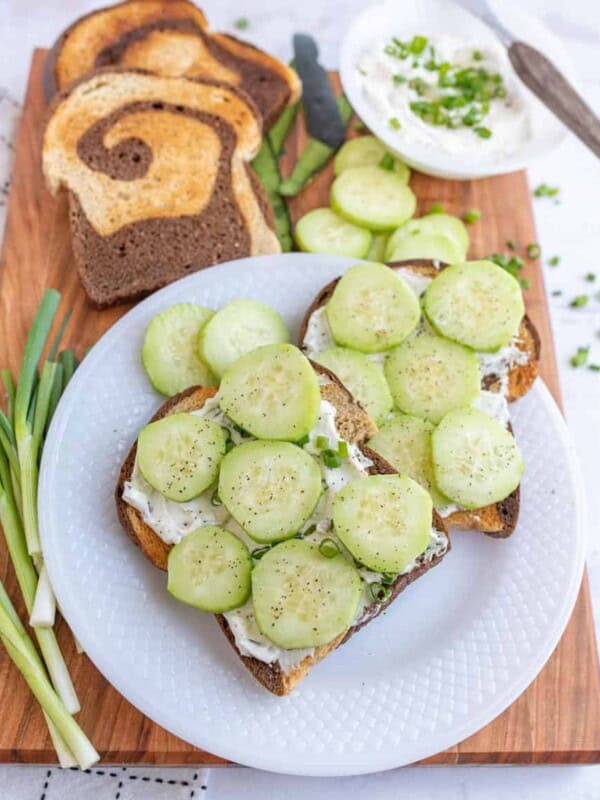 top view of a plate of cucumber sandwiches with the ingredients for them next to the plate