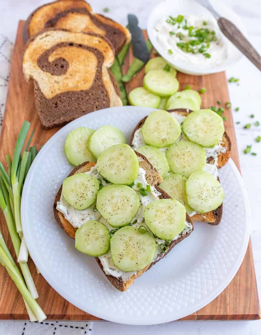 top view of a plate of cucumber sandwiches with the ingredients for them next to the plate