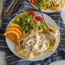 up close picture of a plate of alfredo pasta with salad and orange slices