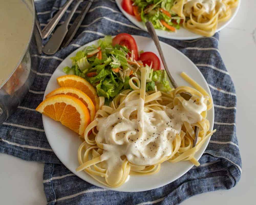 up close picture of a plate of alfredo pasta with salad and orange slices