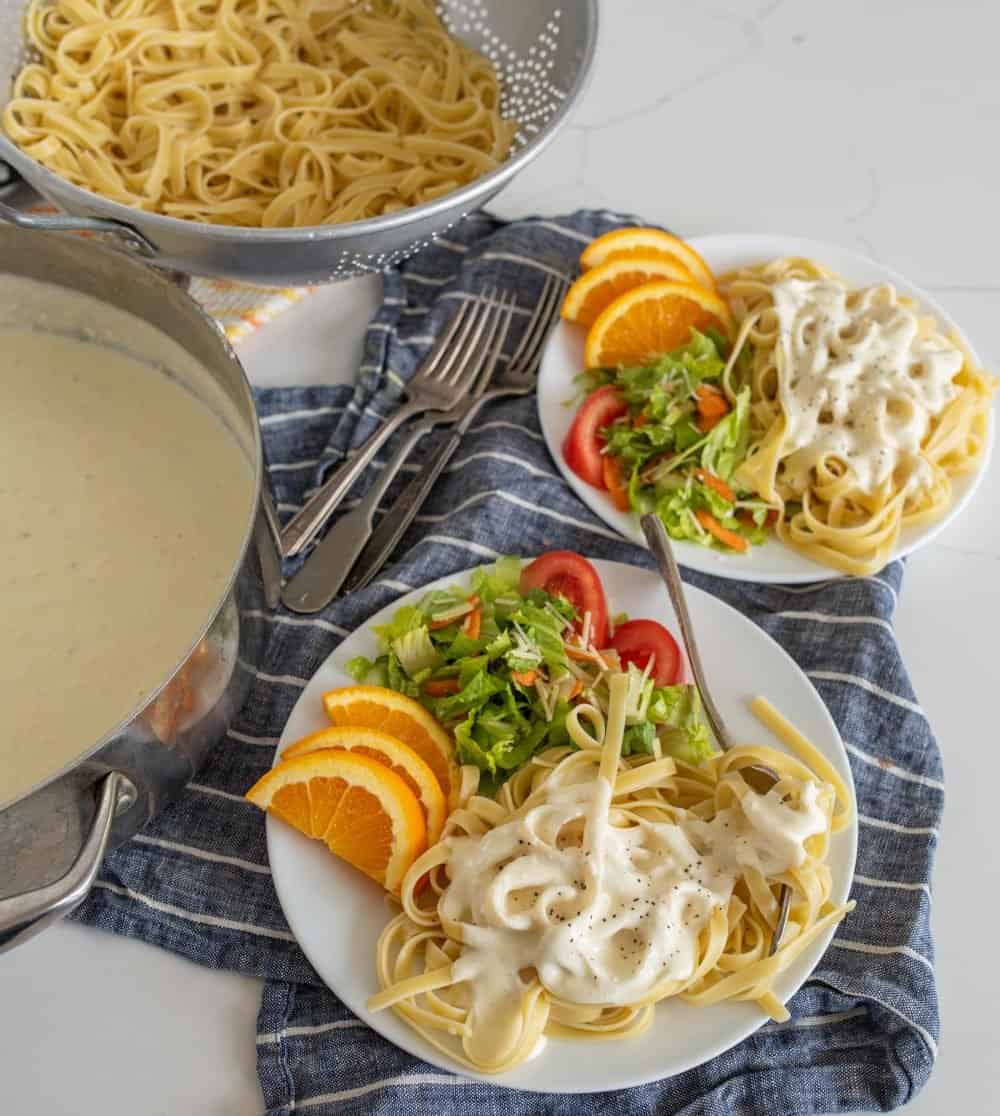 plates of alfredo with salad and orange slices