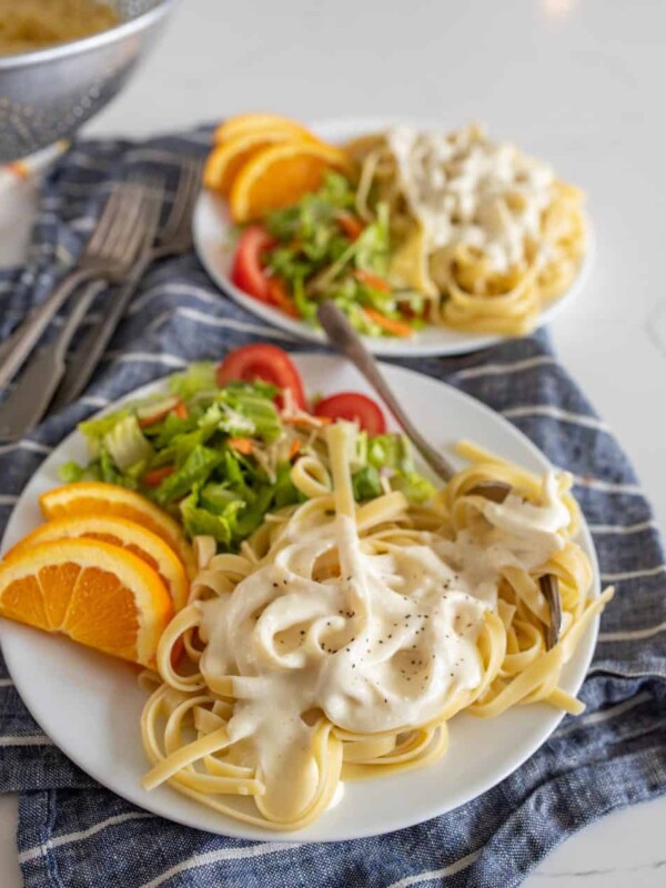 plates of alfredo with salad and orange slices