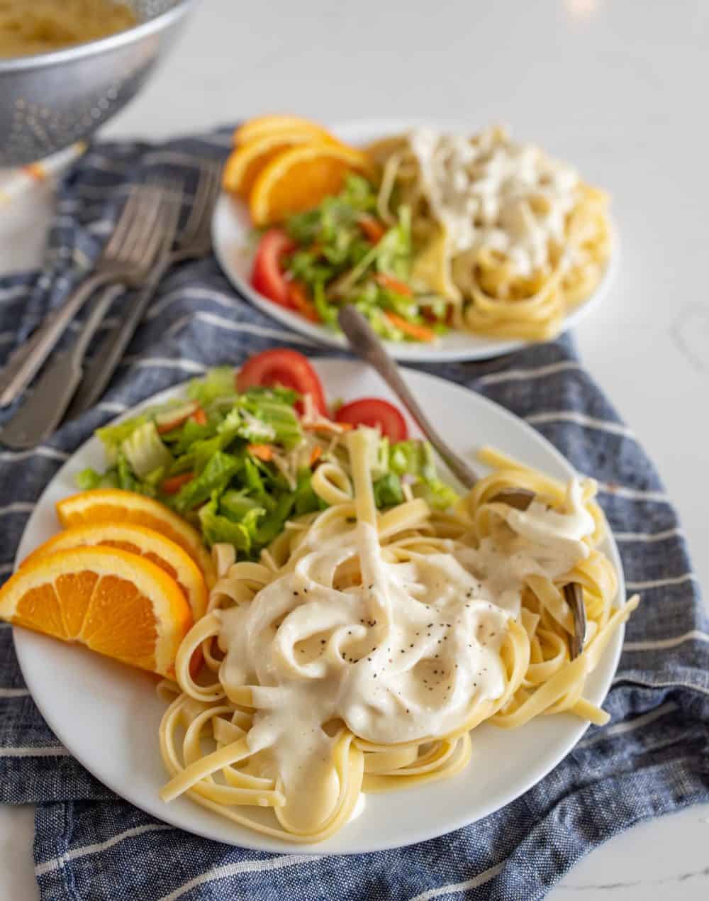 plates of alfredo with salad and orange slices