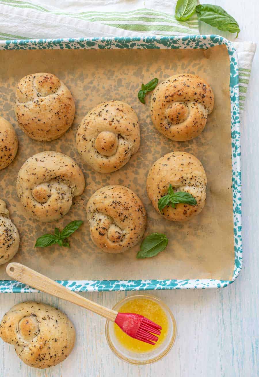 top view of garlic knots on a baking sheet with a bowl of melted butter next to it