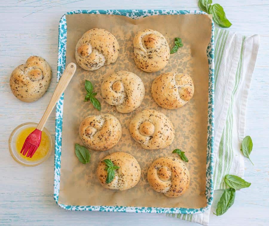 top view of garlic knots on a baking sheet with a bowl of melted butter next to it