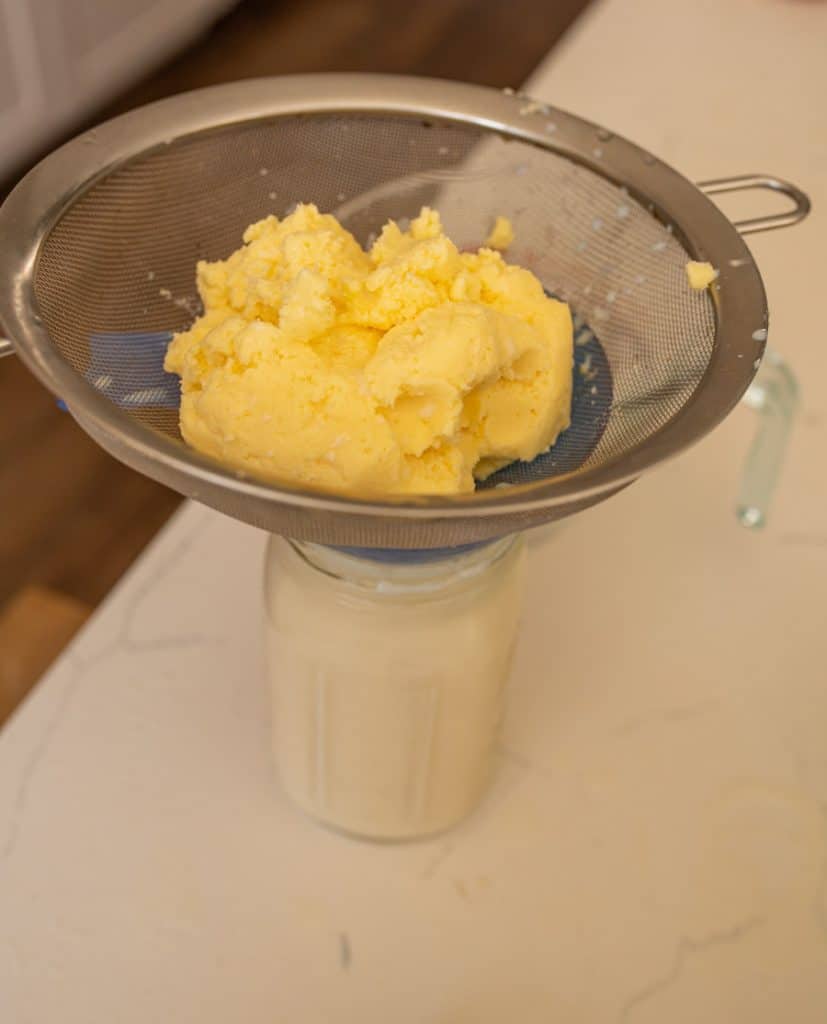 picture of fresh butter in a sieve with a jar of buttermilk underneath
