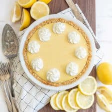 top view of a lemon pie next to lemons and serving utensils