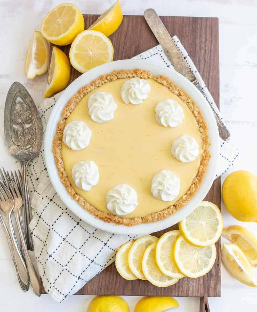 top view of a lemon pie next to lemons and serving utensils