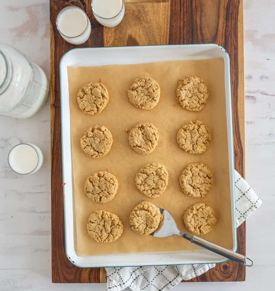 top view of a pan of oatmeal peanut butter cookies with glasses of milk next to them.