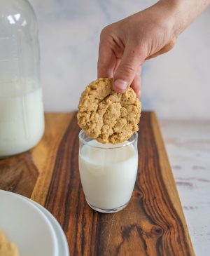 hand dipping oatmeal peanut butter cookie in a glass of milk