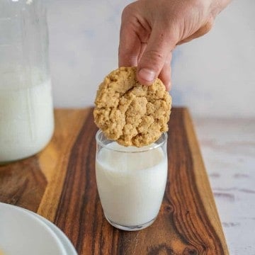 hand dipping oatmeal peanut butter cookie in a glass of milk