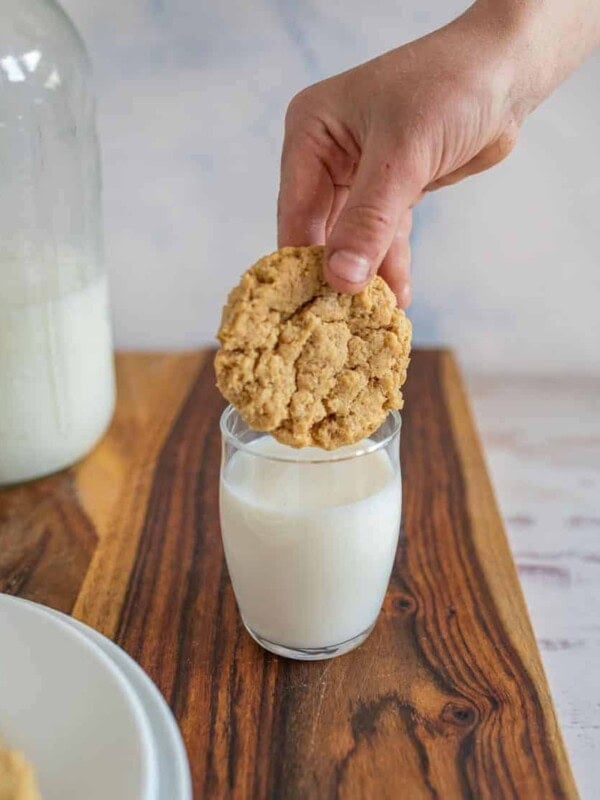 hand dipping oatmeal peanut butter cookie in a glass of milk.