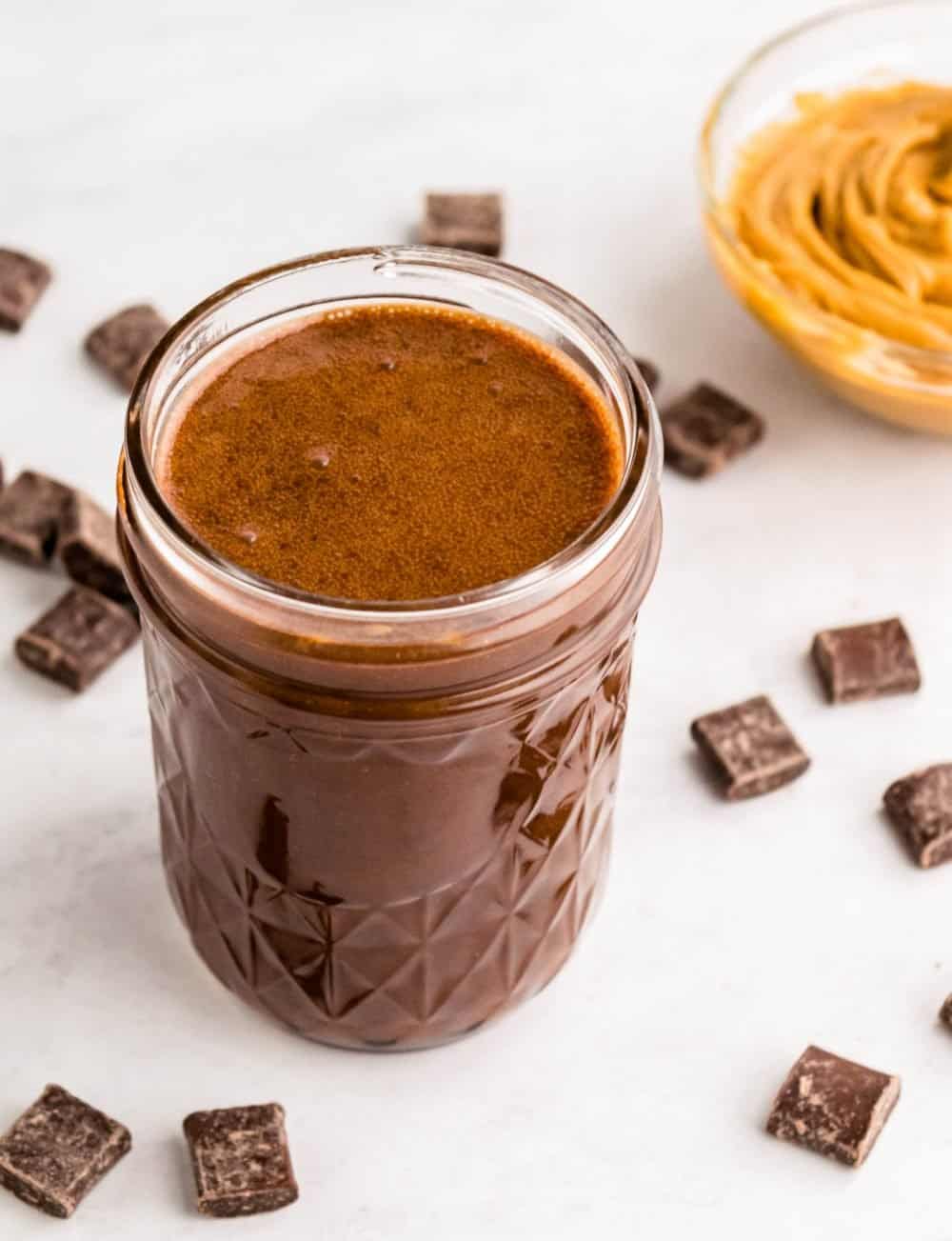 top view of a jar of peanut butter hot fudge with a bowl of peanut butter and chocolate chunks surrounding it