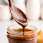 close up picture of a spoon covered in peanut butter hot fudge over a jar of peanut butter hot fudge