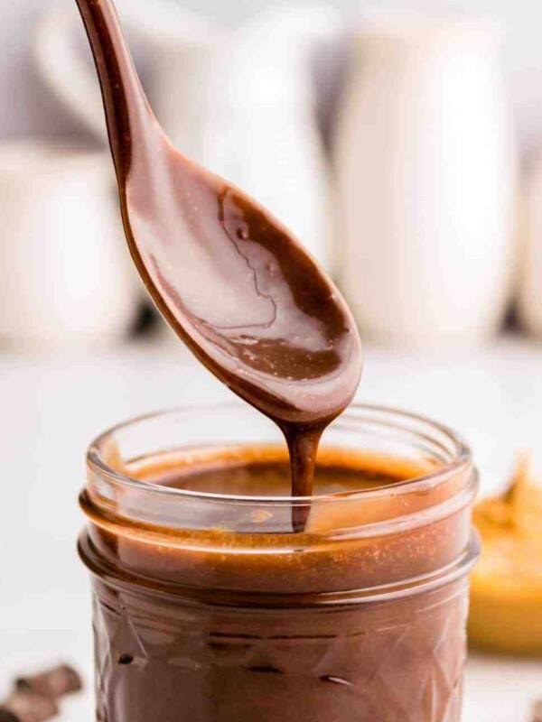 close up picture of a spoon covered in peanut butter hot fudge over a jar of peanut butter hot fudge