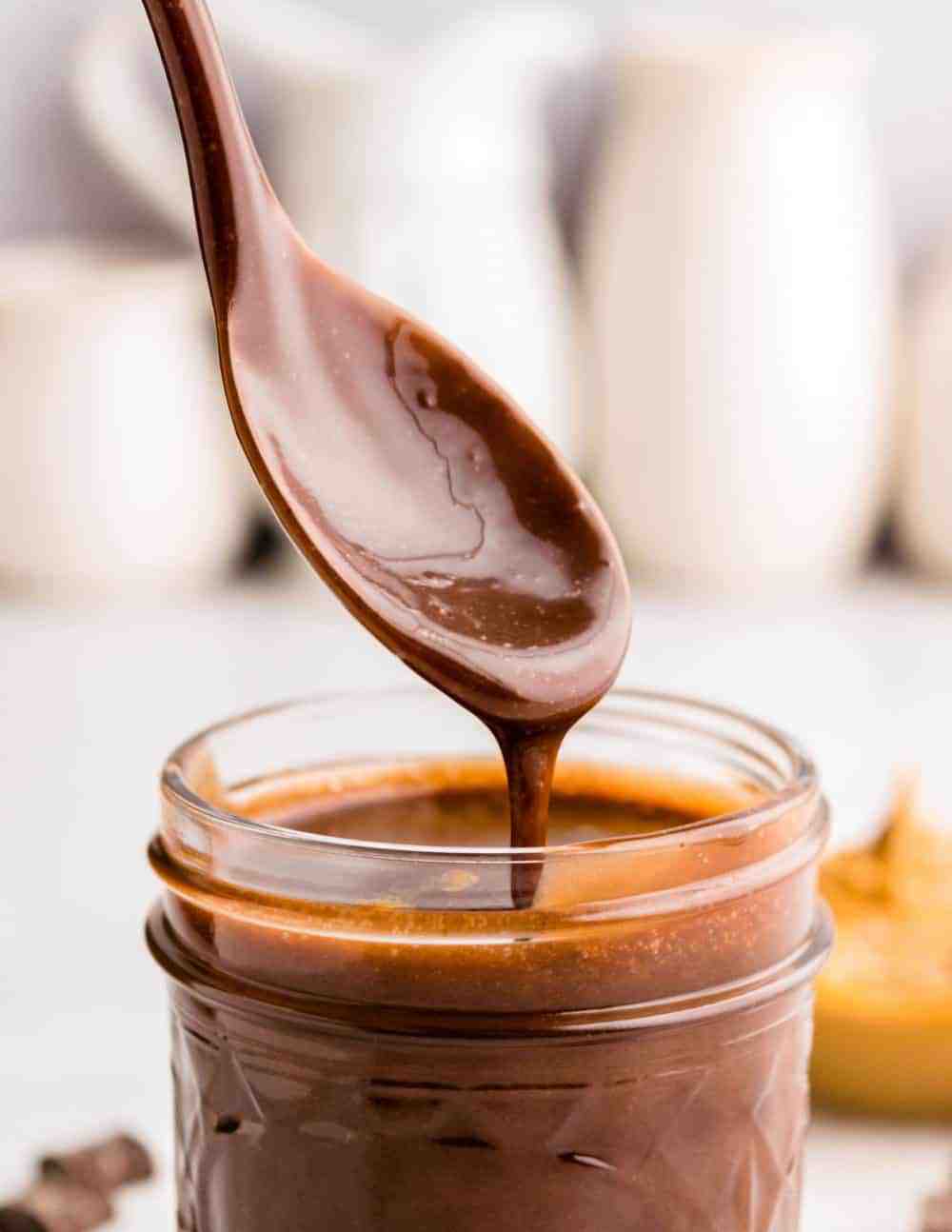 close up picture of a spoon covered in peanut butter hot fudge over a jar of peanut butter hot fudge