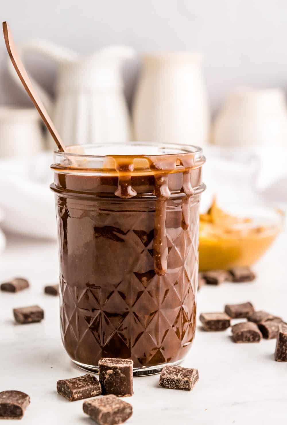 jar of peanut butter hot fudge with chocolate chunks around it