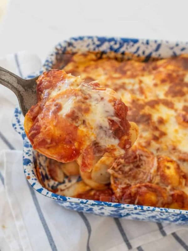 Spoon full of ravioli lasagna, with a baking dish of ravioli lasagna in the background