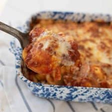 Spoon full of ravioli lasagna, with a baking dish of ravioli lasagna in the background