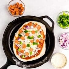 top view of uncooked pizza in a skillet with ingredients in bowls surrounding the skillet