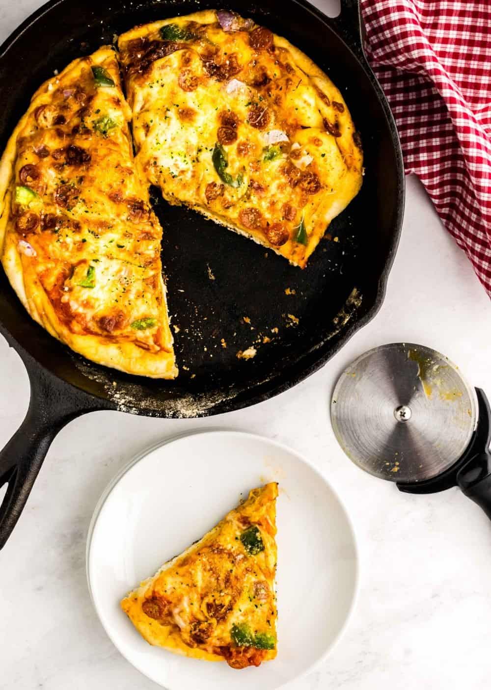 top view of a slice of skillet pizza on a plate with the rest of the pizza in the skillet, next to it