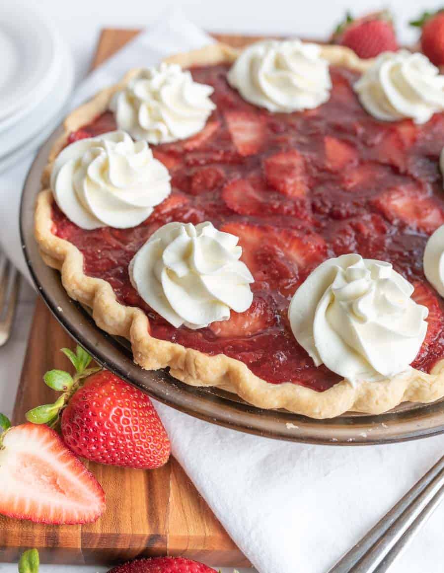 up close picture of a strawberry pie with dollops of whipped cream.