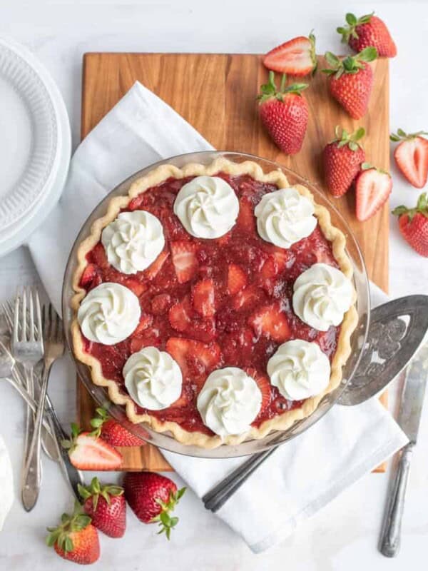 top view of a strawberry pie with strawberries and serving utensils around it