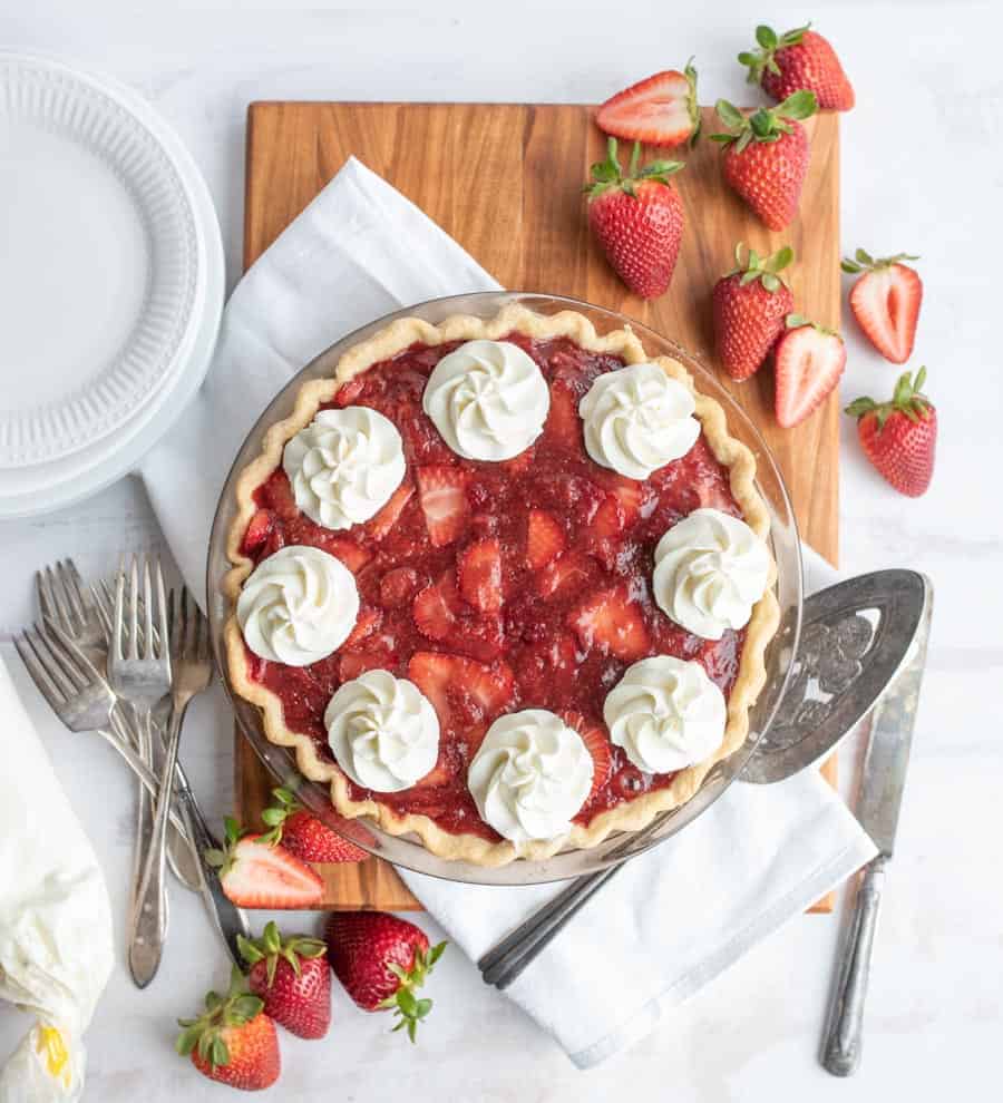 top view of a strawberry pie with strawberries and serving utensils around it.