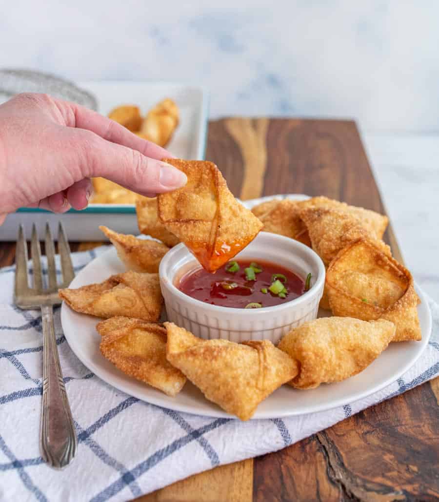 cream cheese wontons being dipped in sauce.