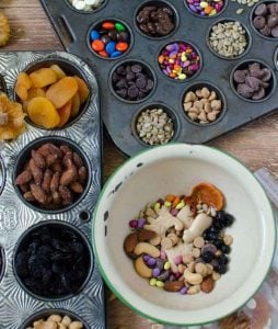 top view of ingredients in a bowl for trail mix next to muffin tins filled with ingredients for trail mix